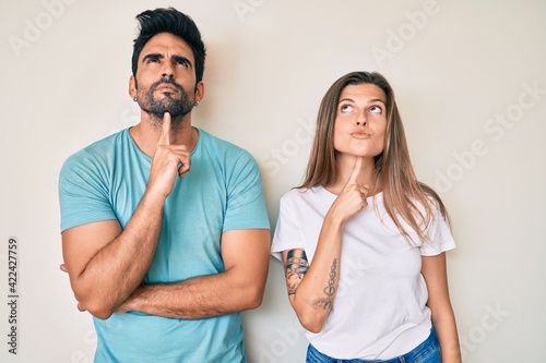 Beautiful young couple of boyfriend and girlfriend together thinking concentrated about doubt with finger on chin and looking up wondering