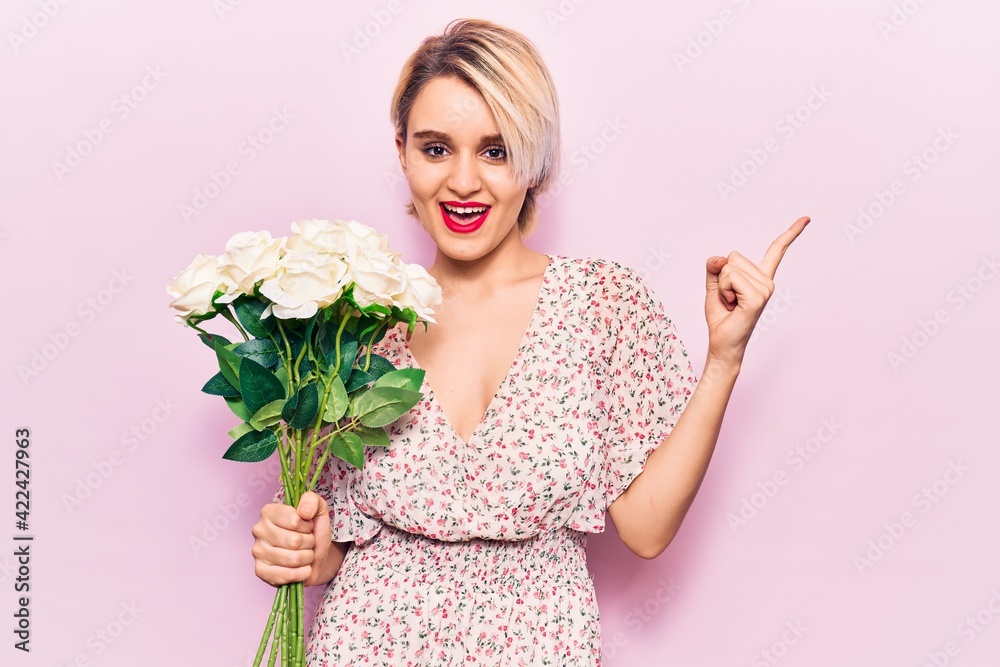 Young beautiful blonde woman holding flowers smiling happy pointing with hand and finger to the side Young beautiful blonde woman holding flowers smiling happy pointing with hand and finger to the side