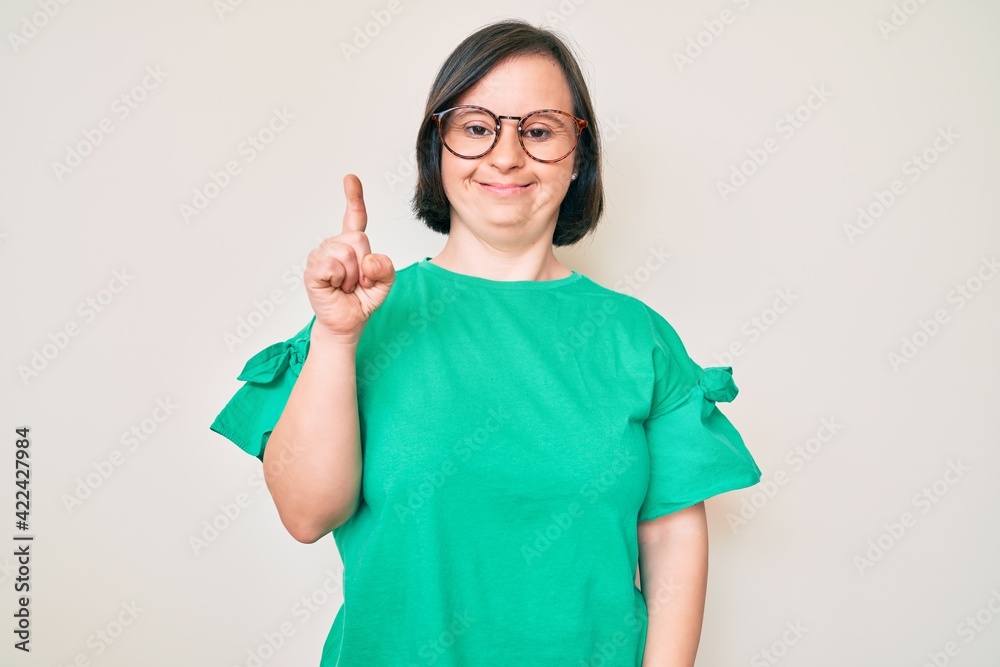 Brunette woman with down syndrome wearing casual clothes and glasses smiling with an idea or question pointing finger up with happy face, number one Brunette woman with down syndrome wearing casual clothes and glasses smiling with an idea or question pointing finger up with happy face, number one