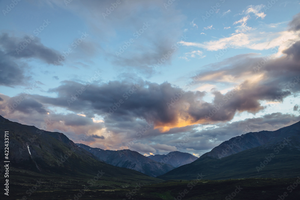 Beautiful mountain scenery with golden dawn light in cloudy sky. Scenic mountain landscape with illuminating color in sunset sky. Silhouettes of mountains on sunrise. Gold illuminating sunlight in sky