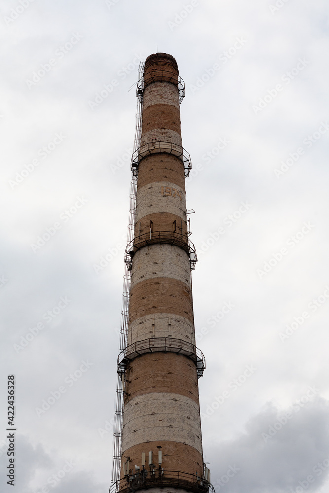 A huge red brick pipe for a gas boiler house built in the USSR was photographed against a cloudy sky.