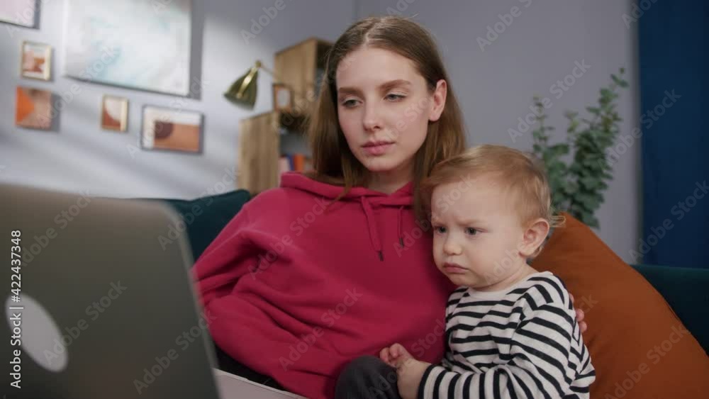 Happy young mother and little son are watching cartoons, being lockdown. Mom and child are sitting on sofa, using laptop. Boy is attentively focusing. Happy young mother and little son are watching cartoons, being lockdown. Mom and child are sitting on sofa, using laptop. Boy is attentively focusing.