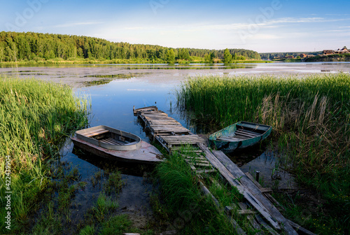 Old boats near a wooden pier in the reeds on the lake near the village in the morning