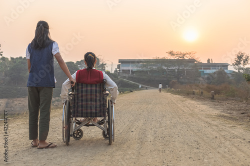 Disabled handicapped woman in wheelchair and care helper walking on trail