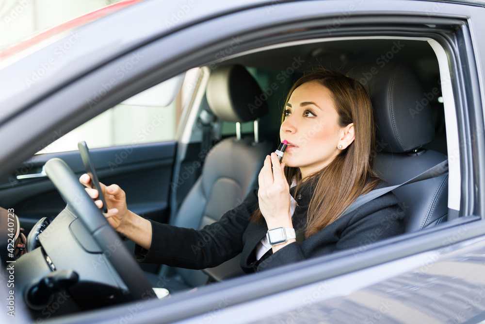 Side view of a beautiful businesswoman putting lipstick in the car