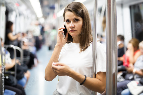 Portrait of young smiling woman using phone standing in subway car