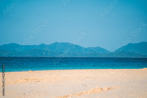Summer tropical beach with clear blue sky and deep blue of water. Focus on mountains in background
