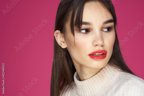 Brunette with long hair red lips cosmetics white sweater pink background cropped view