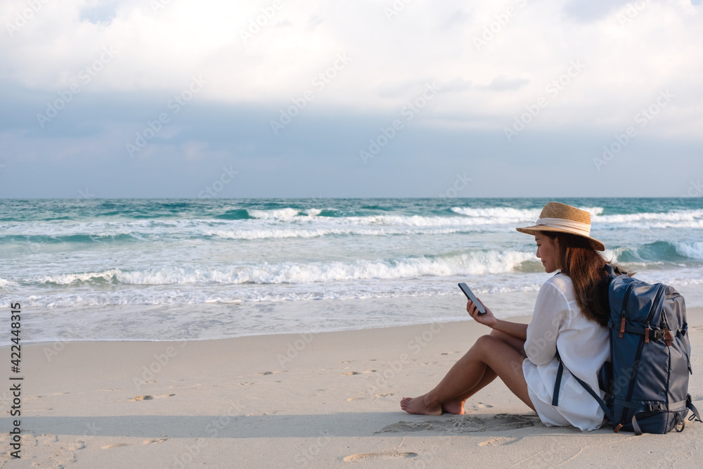 A female traveler holding and using mobile phone while traveling to the sea