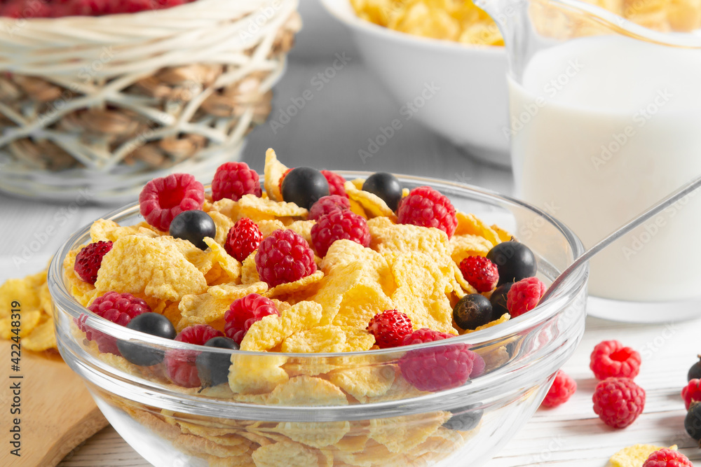 Glass bowl with cereal flakes and berries and milk on the table, close-up. Healthy summer breakfast Glass bowl with cereal flakes and berries and milk on the table, close-up. Healthy summer breakfast