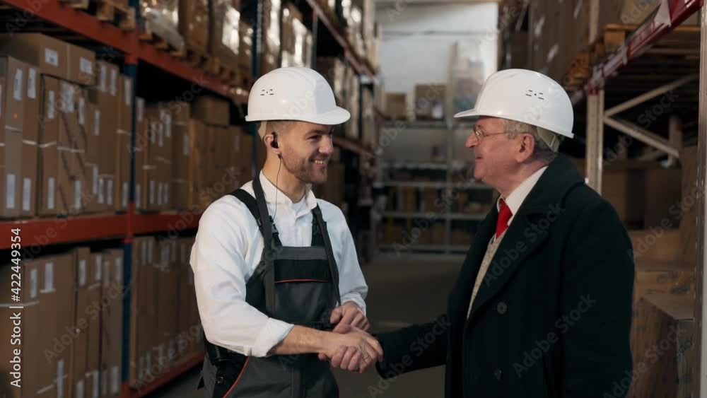 Pleasant handsome man in work uniform with a planet greets an elderly man on the background of a warehouse with boxes Pleasant handsome man in work uniform with a planet greets an elderly man on the background of a warehouse with boxes