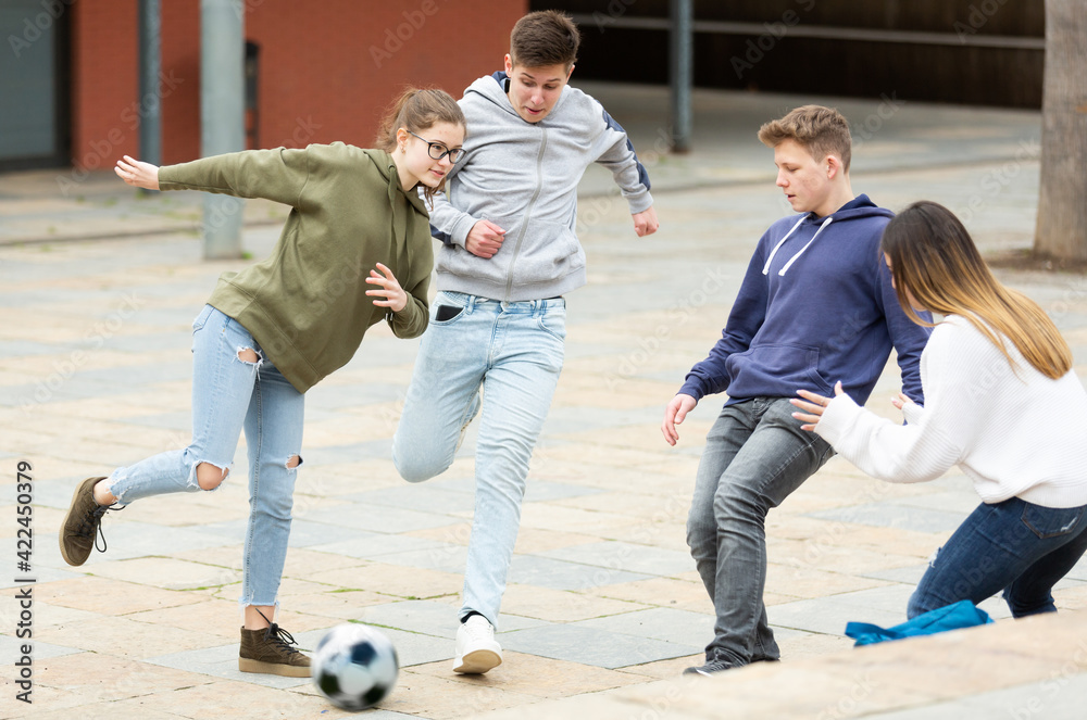 Two teenage boys and two cute girls play ball near the school building