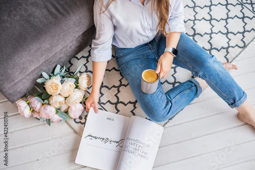 Beautiful natural girl sitting on the floor reading a magazine and drinking coffee, looking down