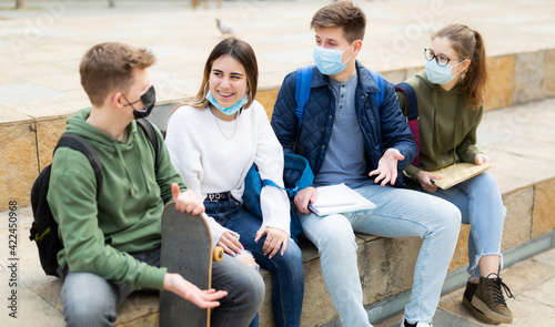 Group of modern cheerful teenagers in protective masks having fun spending time together