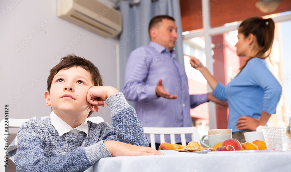 Obraz premium Portrait of unhappy preteen boy sitting at home while parents quarreling..