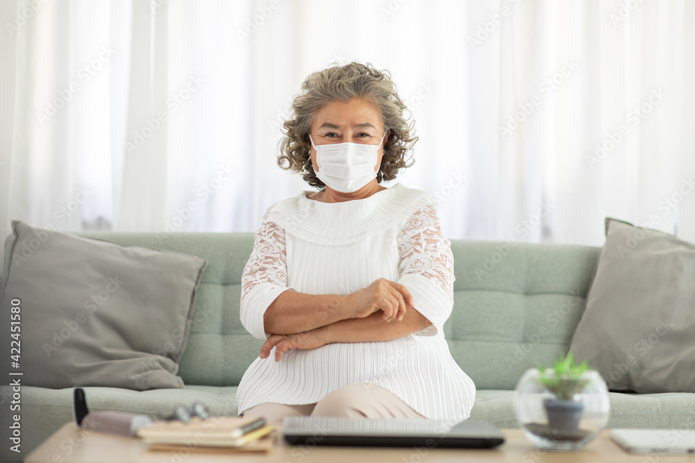 Happy Asian Elderly or Seniors woman wearing medical mask to prevent coronavirus sitting on sofa in living room at home,New normal lifestyle of older stay at home Happy Asian Elderly or Seniors woman wearing medical mask to prevent coronavirus sitting on sofa in living room at home,New normal lifestyle of older stay at home