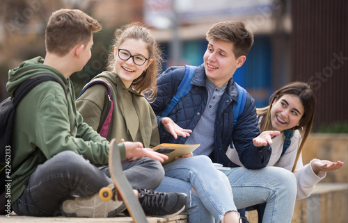 Schilderij op canvas Smiling cheerful teenagers talking with each other sitting on stairs on city str