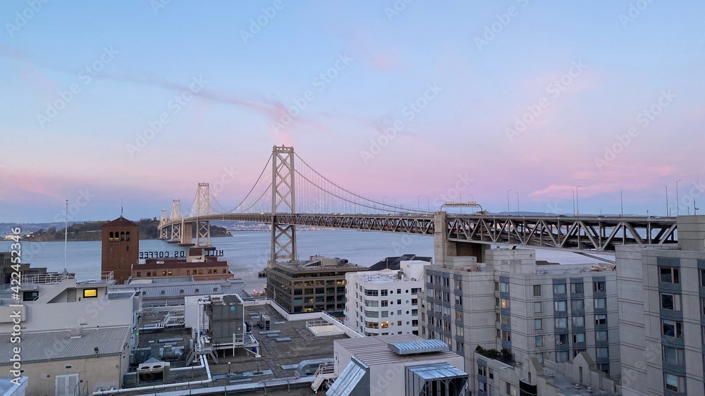 View of the San Francisco Bay Bridge from the East Cut (South of Market Street) neighborhood of San Francisco during sunset in the Spring of 2021. View of the San Francisco Bay Bridge from the East Cut (South of Market Street) neighborhood of San Francisco during sunset in the Spring of 2021.