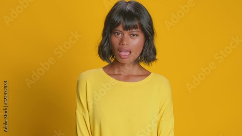 Astonished young woman looks amazement stares disbelief over yellow background