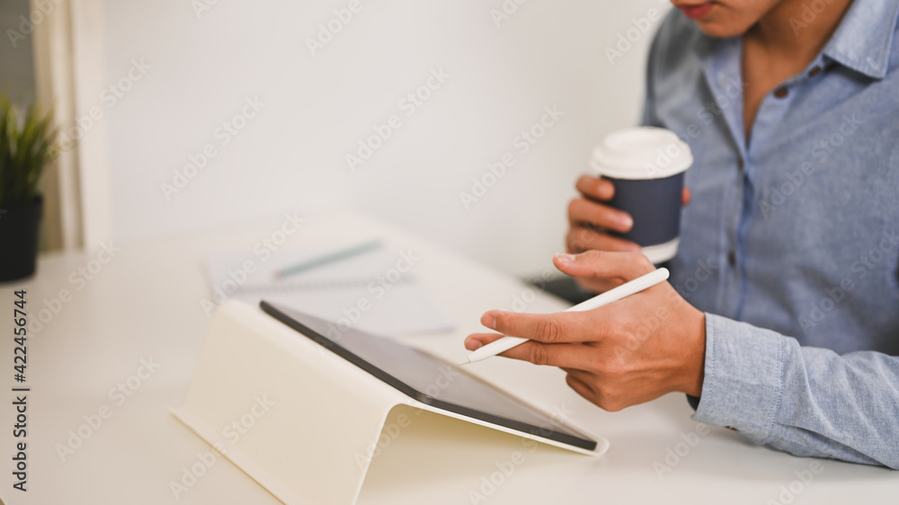Fototapeta premium Cropped shot of businessman holding cup of hot beverage and working with digital tablet.