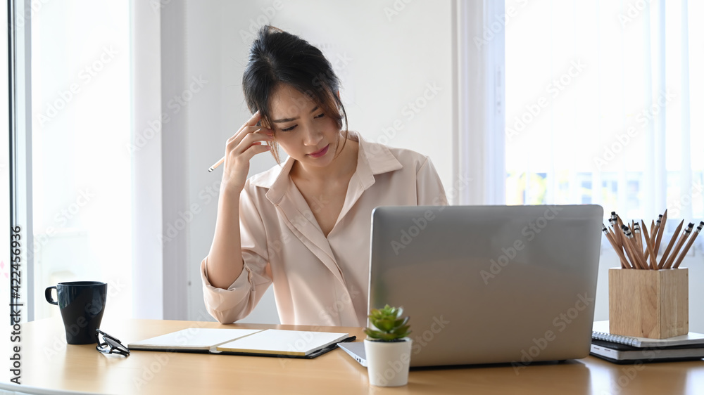 Stressed businesswoman sitting in office desk holding her head and looking at screen of laptop computer. Stressed businesswoman sitting in office desk holding her head and looking at screen of laptop computer.