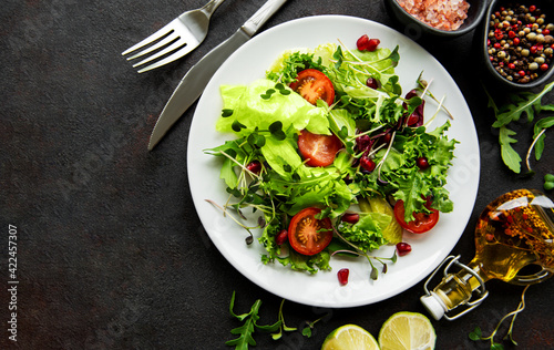 Fresh green mixed  salad bowl with tomatoes and microgreens  on black concrete background. Healthy food, top view.