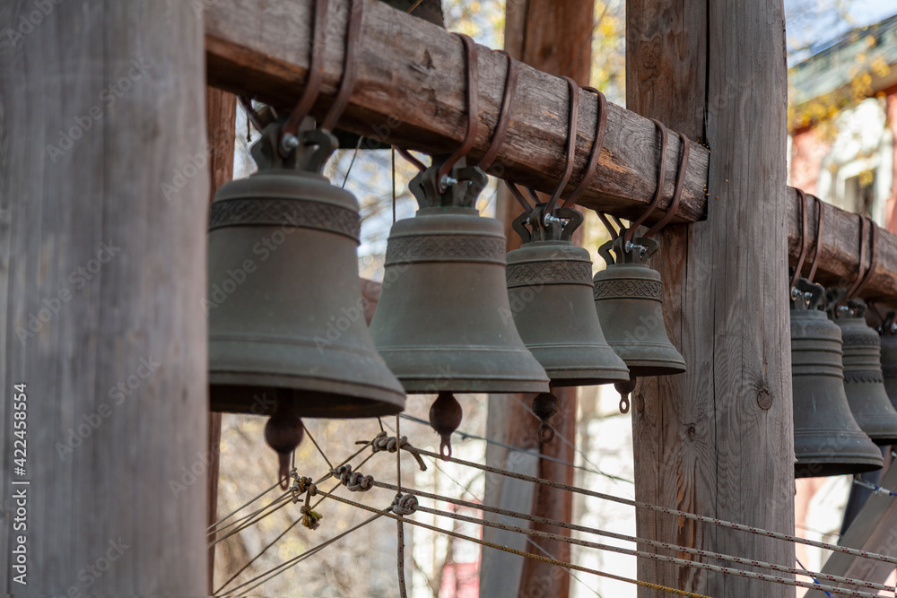 A group of bronze church bells hang in a row on a wooden beam A group of bronze church bells hang in a row on a wooden beam