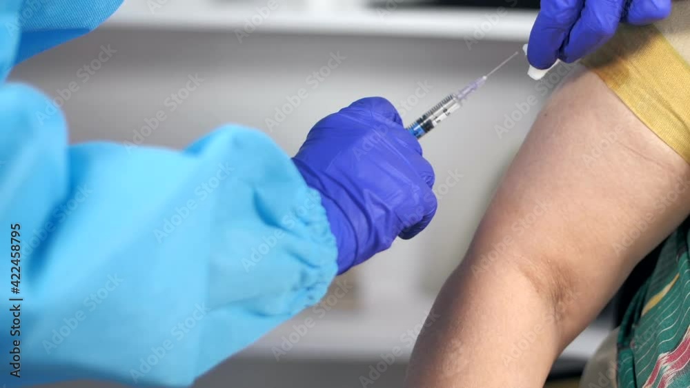 A medical worker in safety gloves and PPE Kit injecting corona vaccine . Extreme closeup shot of a doctor's hand wearing PPE suit vaccinating a woman - new effective COVID-19 shot treatment