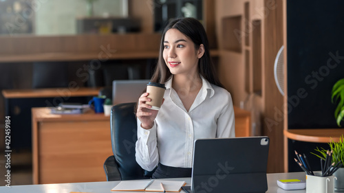 Asian businesswoman drinking coffee with tablet on desk at office.