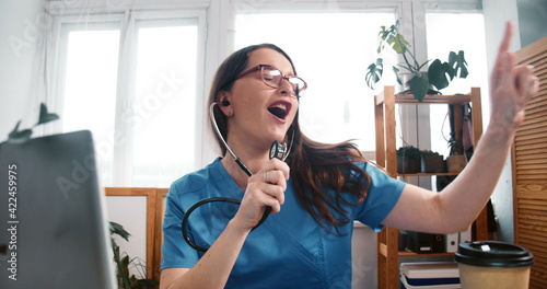 Zoom out on fun young happy scientist doctor woman dancing, singing at lab work table celebrating with food and coffee.
