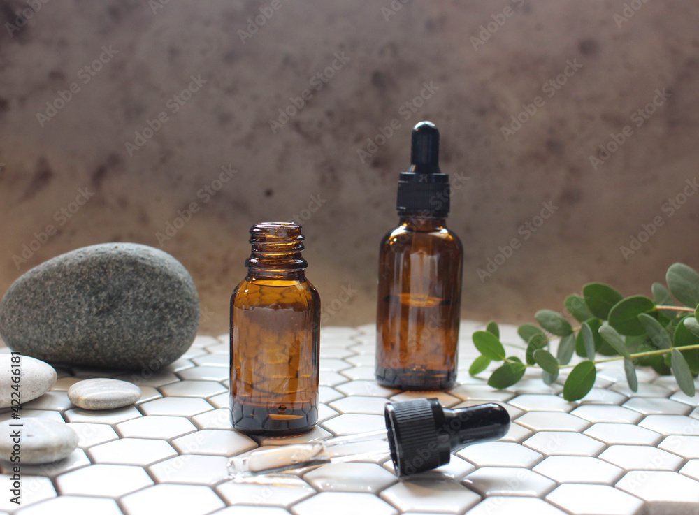 A glass bottle with aromatic oil or serum on a stone and little twig with flowers near. Natural Organic Spa Cosmetic concept. Front view. A glass bottle with aromatic oil or serum on a stone and little twig with flowers near. Natural Organic Spa Cosmetic concept. Front view.