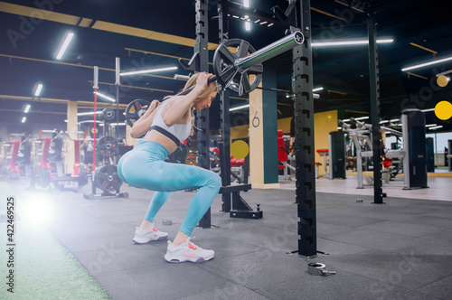 Beautiful sports fitness girl with a barbell. Sporty woman exercising with barbell in gym.