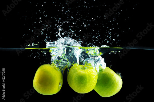 Green apples falling into the water with a splash against black background