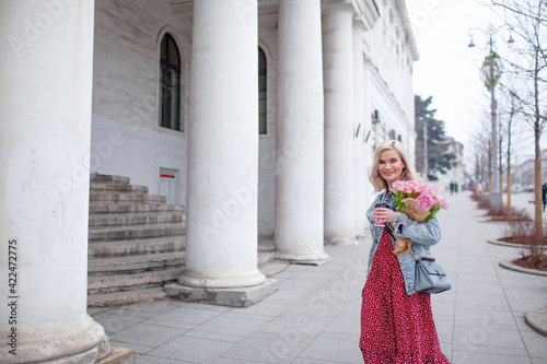 Beautiful woman in fashion clothes walking in the street with bouquete of flowers and coffee or tea to go © Вероника Зеленина