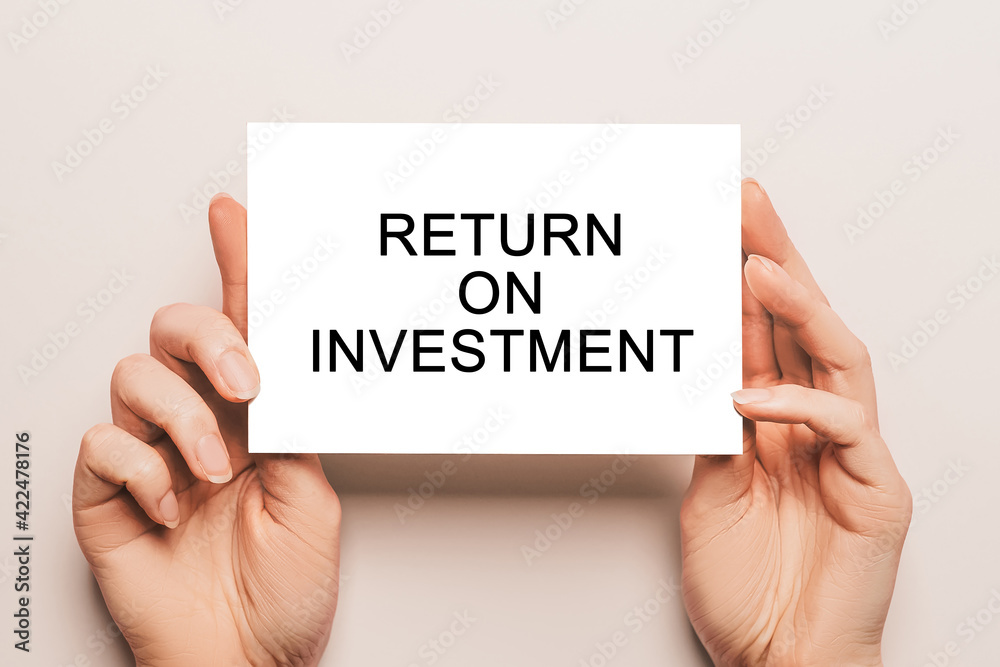 Female hands hold card paper with text Return on Investment on a yellow background. Business and finance concept Female hands hold card paper with text Return on Investment on a yellow background. Business and finance concept