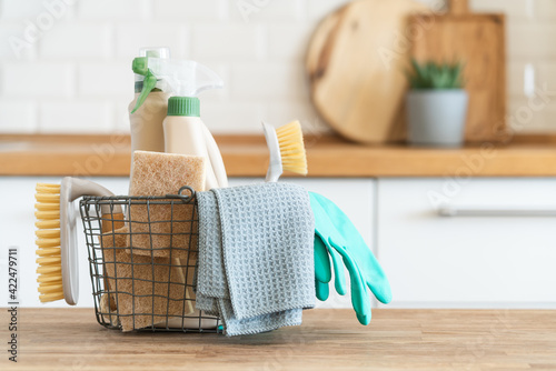 Basket with brushes, rags, natural sponges and cleaning products. Modern kitchen interior in the background. House cleaning concept