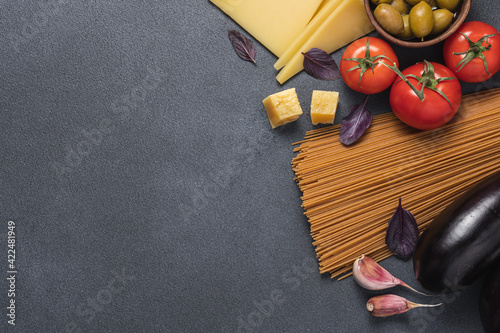 Ingredients for making spaghetti with eggplant. Whole grain pasta, vegetables, parmesan cheese, garlic, olives, red basil. Mediterranean food cooking background