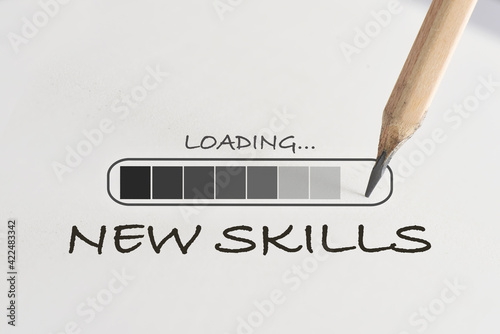 New skills loading written on white paper with processing symbol and pencil. Reskilling and upskilling concept with power of learning idea