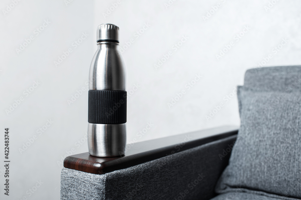 Close-up of steel reusable thermo water bottle on sofa, against grey wall. Close-up of steel reusable thermo water bottle on sofa, against grey wall.