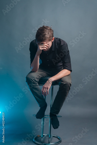 Sad guy sits on a bar stool on a gray background © ISliM