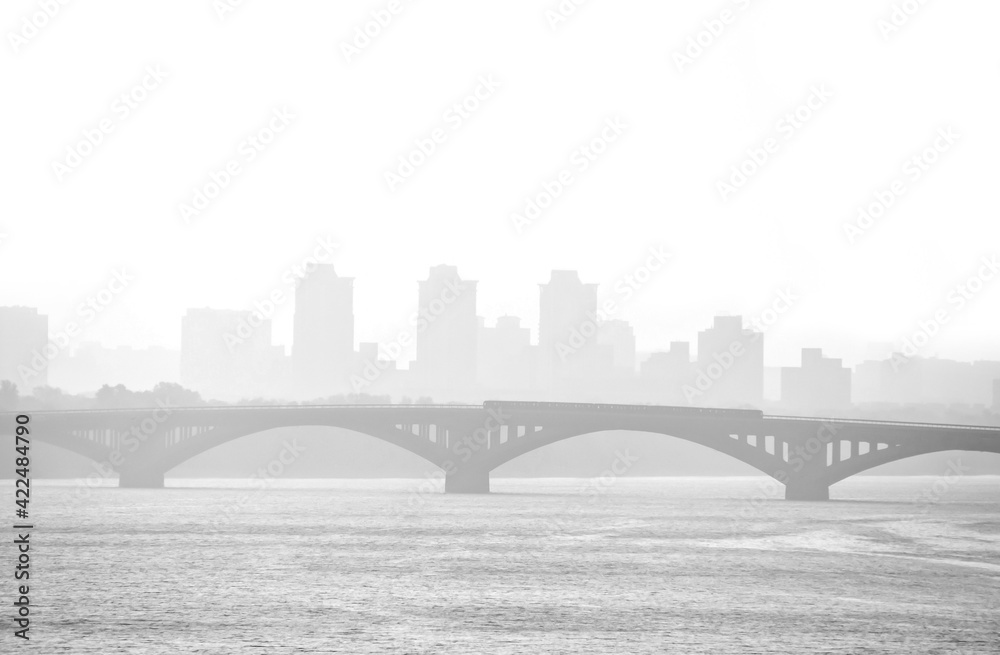 Train traveling on the bridge over the river Dnipro foggy morning. Bridge over river in misty morning. Kiev skyline silhouette. The Metro bridge in Kiev with fog and silhouette of city in background.
