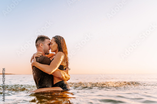 Happy young fit couple in sea or ocean hug each other with love at summer sunset. Romantic mood, tenderness, relationship, vacation concept. © Olga
