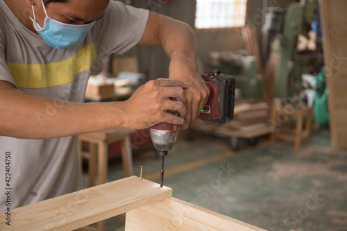 Close-up of carpenter using electric drill in workshop and routing out holes Cabinetmaker drilling wood on table. Joinery work on the production and renovation of wooden furniture. Small Business