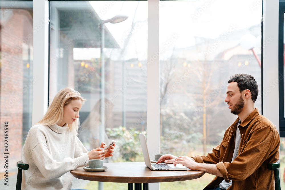 Focused man and woman using laptop and cellphone while drinking coffee Focused man and woman using laptop and cellphone while drinking coffee