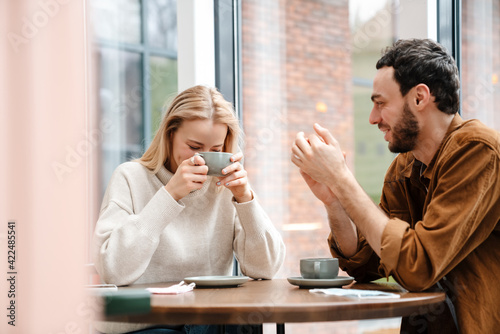 Young man and woman smiling and talking while drinking coffee in cafe