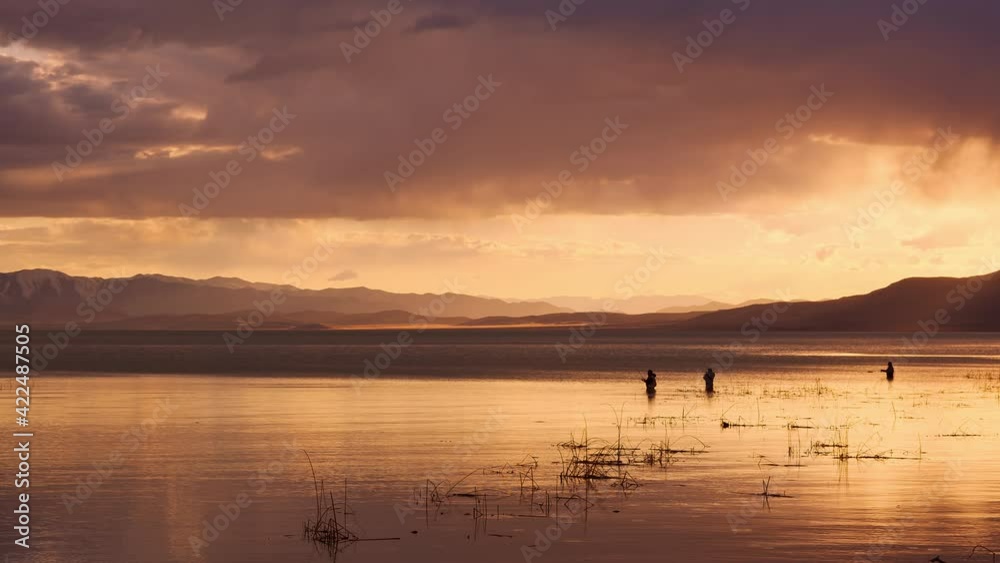 Rain falling in the distance past fishermen standing in Utah Lake during sunset. Rain falling in the distance past fishermen standing in Utah Lake during sunset.