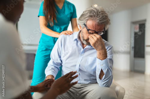 Female doctor reassuring supporting senior adult patient in hospital. Kind caring young woman nurse or caregiver helping older retired man talking, giving comfort, expressing care concept.