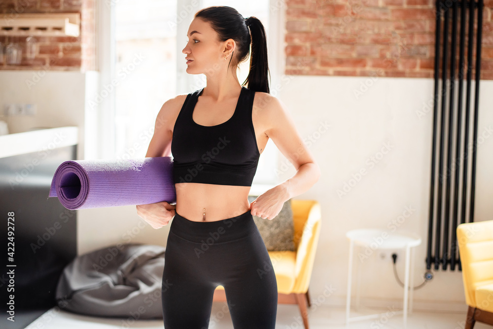 Attractive woman with slender body holding yoga mat