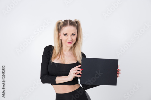 A beautiful blonde in black clothes holds a sheet of black paper in her hands. 