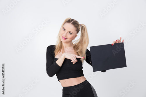A beautiful blonde in black clothes holds a sheet of black paper in her hands. 